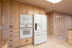 Kitchen featuring white appliances,  two ovens, light tile patterned flooring, granite countertops, and beautiful cabinets