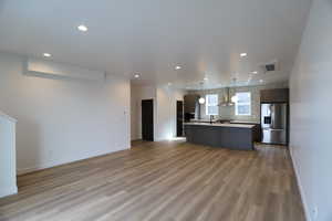 Kitchen featuring open floor plan, stainless steel refrigerator with ice dispenser, a center island with sink, light countertops, and hanging light fixtures
