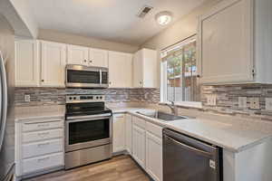 Kitchen featuring appliances with stainless steel finishes, light countertops, white cabinets, a textured ceiling, and light wood-style floors