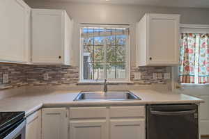 Kitchen with white cabinetry, dishwasher, light countertops, and tasteful backsplash