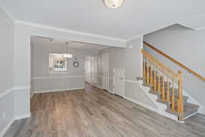 Unfurnished living room featuring stairs, ornamental molding, wood finished floors, and a textured ceiling