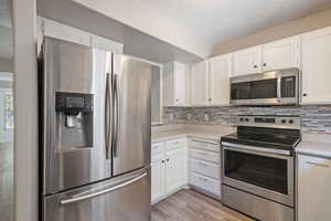 Kitchen featuring stainless steel appliances, white cabinets, a textured ceiling, tasteful backsplash, and light wood-style floors