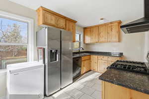 Kitchen with extractor fan, black appliances, light brown cabinetry, dark stone countertops, and light tile patterned floors