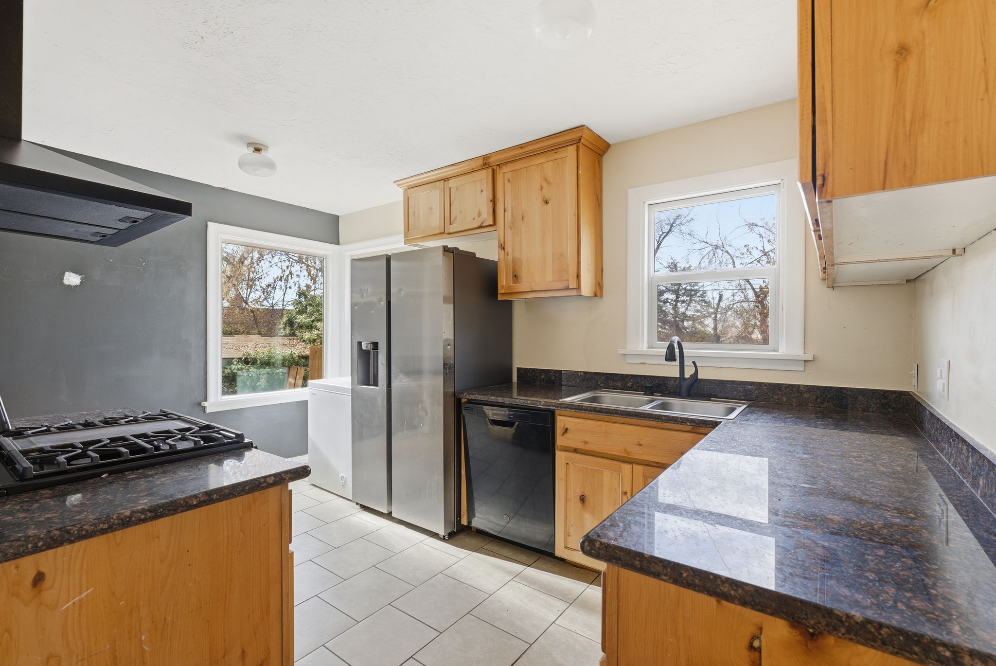Kitchen with exhaust hood, black appliances, healthy amount of natural light, and dark stone counters