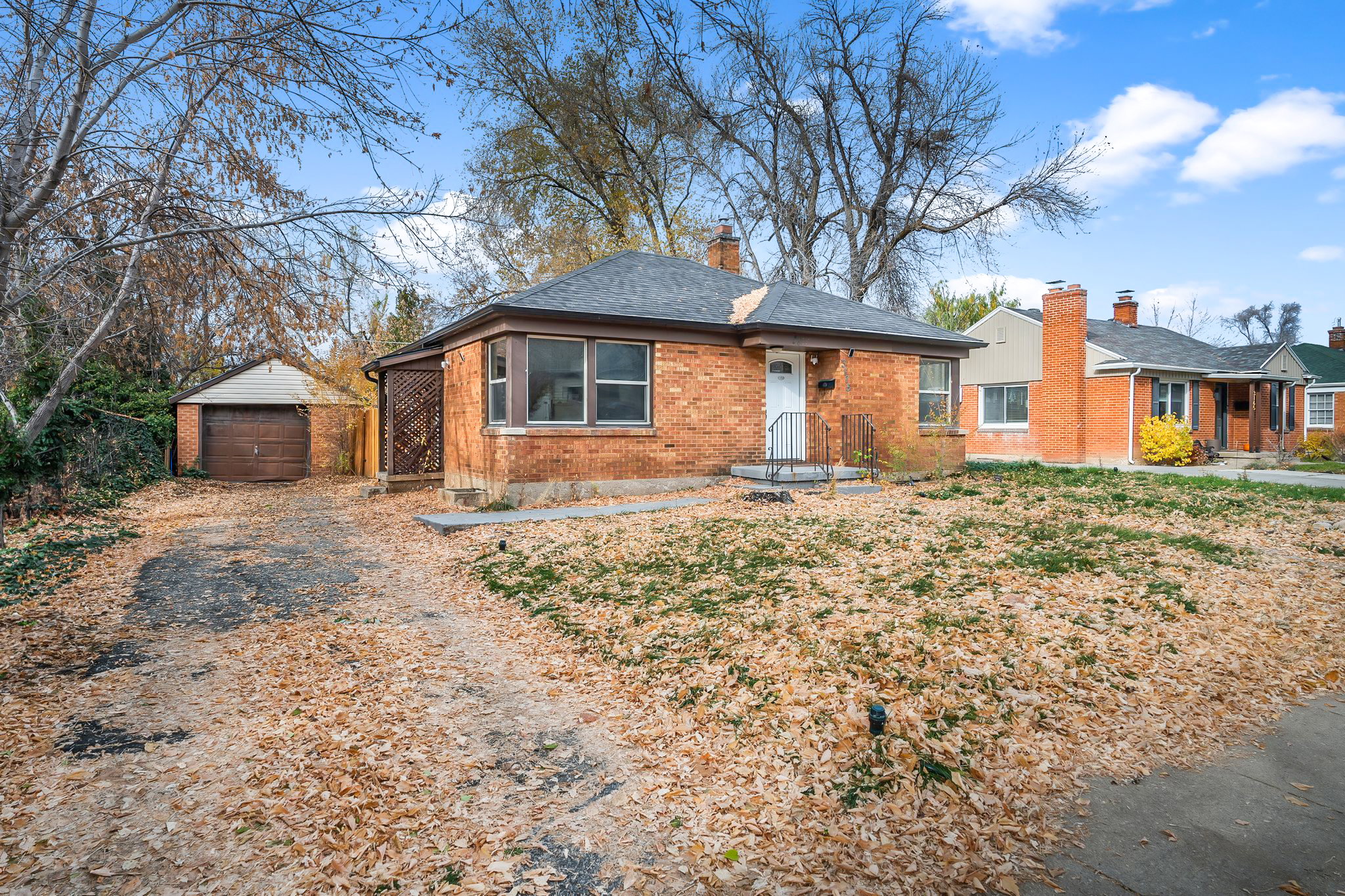 Single story home with an outdoor structure, driveway, brick siding, a chimney, and a garage