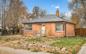 Bungalow with a shingled roof, a chimney, and brick siding