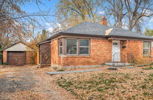 View of front facade with a chimney, a shingled roof, an outdoor structure, brick siding, and driveway