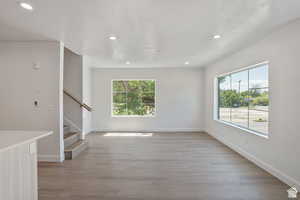 Unfurnished living room featuring light wood finished floors, plenty of natural light, stairs, and recessed lighting