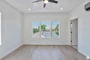 Spare room with light wood-type flooring, a wall mounted air conditioner, ceiling fan, and recessed lighting