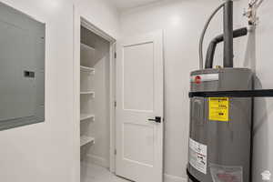 Utility room featuring electric panel and strapped water heater