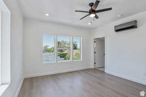 Unfurnished room with light wood-style flooring, a wall unit AC, ceiling fan, and recessed lighting