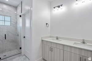 Full bathroom with double vanity, light marble finish floors, and a stall shower