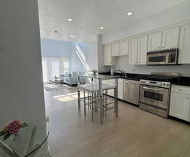 Kitchen featuring a textured ceiling, appliances with stainless steel finishes, recessed lighting, light wood-style floors, and white cabinetry