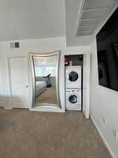 Laundry area with carpet floors, stacked washing machine and dryer, and a textured ceiling