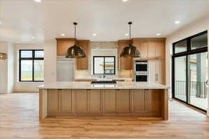 Kitchen featuring light stone countertops, a spacious island, appliances with stainless steel finishes, pendant lighting, and light wood-style floors