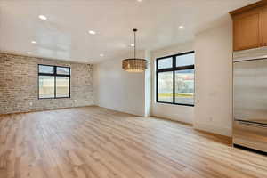 Unfurnished dining area featuring brick wall, light wood finished floors, recessed lighting, a chandelier, and an accent wall