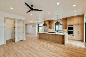 Kitchen with a large island, decorative light fixtures, stainless steel double oven, a ceiling fan, and light wood finished floors