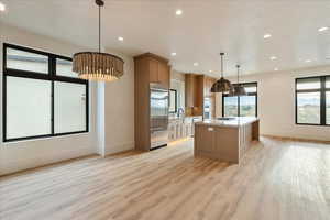 Kitchen featuring decorative light fixtures, a kitchen island, light stone countertops, light wood-style flooring, and appliances with stainless steel finishes