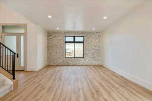 Unfurnished room featuring brick wall, stairs, light wood finished floors, an accent wall, and recessed lighting