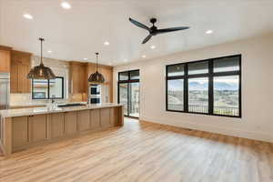 Kitchen with a large island with sink, light wood-style flooring, decorative light fixtures, light stone counters, and ceiling fan