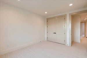 Unfurnished bedroom featuring light carpet, a closet, and recessed lighting