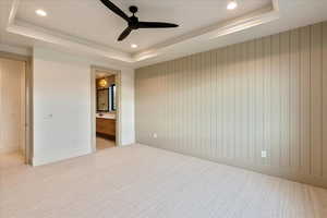 Unfurnished bedroom with a raised ceiling, recessed lighting, wood walls, light colored carpet, and ensuite bathroom