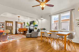 Dining space featuring light wood-style floors, a fireplace, a chandelier, and ceiling fan