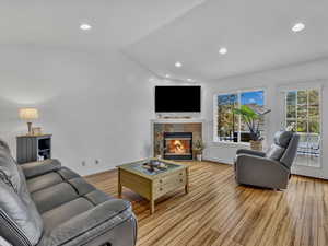Living room featuring vaulted ceiling, light wood finished floors, a tile fireplace, and recessed lighting, electric blinds