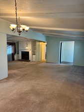 Unfurnished living room featuring carpet floors, a fireplace with raised hearth, a textured ceiling, and a chandelier