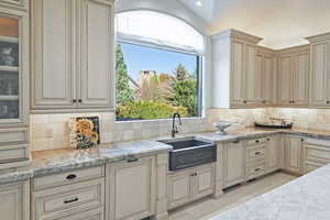 Kitchen featuring cream cabinetry, decorative backsplash, light stone countertops, and light tile patterned floors