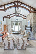 Living area featuring a chandelier, high vaulted ceiling, a stone fireplace, beamed ceiling, and recessed lighting