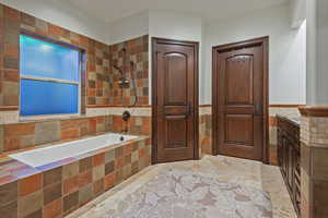 Full bath with wainscoting, tiled shower / bath, vanity, and tile walls