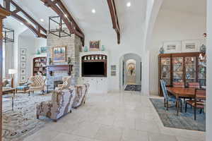 Living area featuring high vaulted ceiling, arched walkways, a stone fireplace, beamed ceiling, and recessed lighting