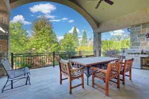 View of patio with outdoor dining space, a ceiling fan, a grill, and view of wooded area