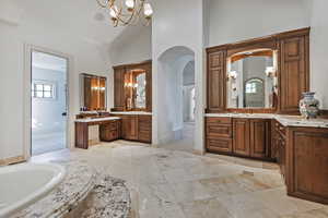 Bathroom featuring a chandelier, two vanities, high vaulted ceiling, and a bathtub
