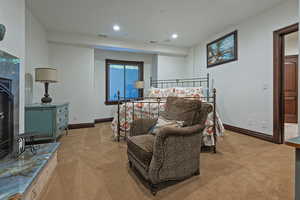 Bedroom with light colored carpet, recessed lighting, and a fireplace with raised hearth