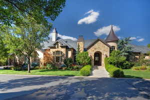 French provincial home with stone siding, a front lawn, a high end roof, a chimney, and stucco siding