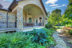 Entrance to property with a ceiling fan, stone siding, and stucco siding