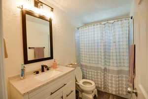 Bathroom with a textured wall, vanity, and a textured ceiling