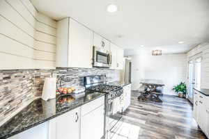 Kitchen with appliances with stainless steel finishes, white cabinetry, dark stone counters, light wood-type flooring, and wooden walls