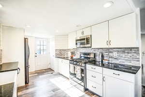 Kitchen featuring stainless steel appliances, white cabinets, dark stone counters, recessed lighting, and light wood finished floors