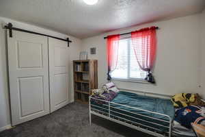 Bedroom featuring a barn door, a textured ceiling, dark colored carpet, and a closet