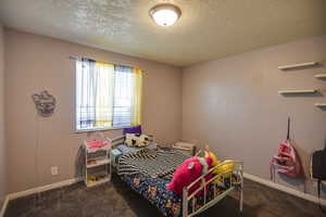 Bedroom with a textured ceiling and dark carpet