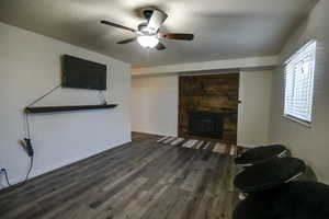 Living room with dark wood-type flooring, a stone fireplace, and ceiling fan