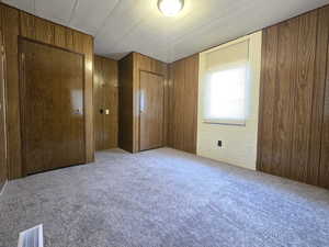 Unfurnished bedroom with light carpet, wooden walls, and a closet