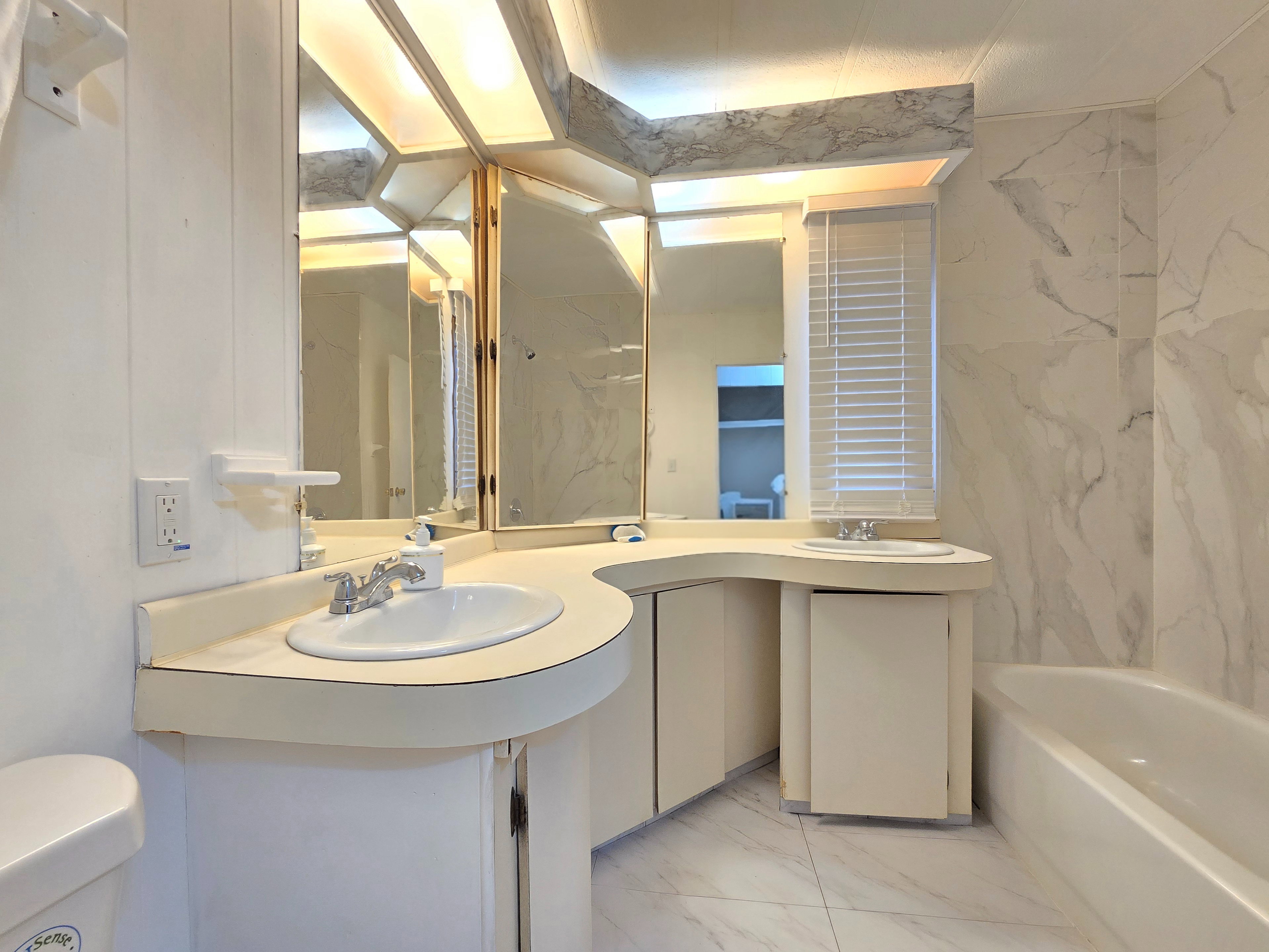 Full bathroom with light marble finish flooring, double vanity, a bath, and stone wall