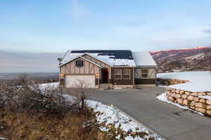 English style home with brick siding, concrete driveway, board and batten siding, roof mounted solar panels, and a garage