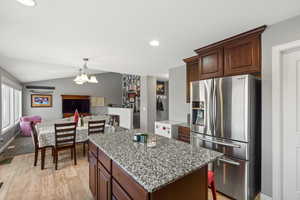 Kitchen with stainless steel fridge with ice dispenser, light stone counters, dark brown cabinets, open floor plan, and a kitchen island