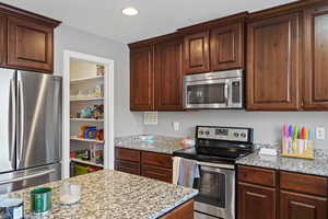 Kitchen with appliances with stainless steel finishes, light stone counters, and dark brown cabinetry