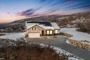 View of front facade featuring brick siding, driveway, board and batten siding, a garage, and roof mounted solar panels